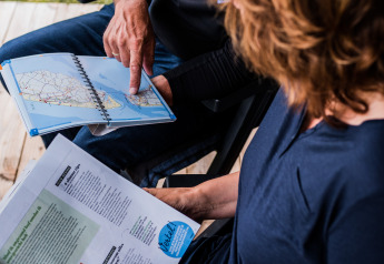 Twee personen bekijken een kaart en brochure samen op Nommerlayen Lodge, Luxemburg, in openlucht.