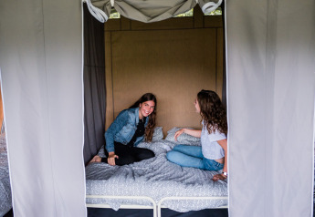 Due giovani donne sorridono e chiacchierano sedute su un letto in una lodge, circondate da tende.