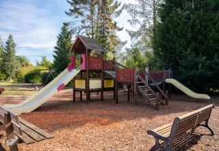 Speeltuin met glijbanen en houten speeltoestel in een bosrijke omgeving bij vakantiepark Overijssel.