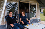 Dos personas están sentadas frente a una casa de campaña, disfrutan de un juego de mesa y jugo en la mesa.