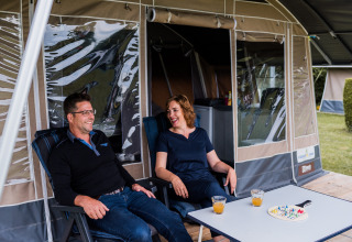 Due persone si rilassano davanti a una tenda lodge, bevono succo e giocano a un gioco da tavolo sul tavolo.