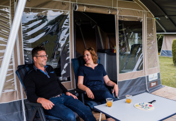 Due persone si rilassano davanti a una tenda lodge, bevono succo e giocano a un gioco da tavolo sul tavolo.
