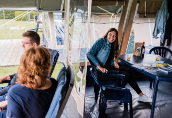 Drie personen relaxen in een lodge tent, met stoelen en drankjes, tijdens een gezellige campingvakantie.