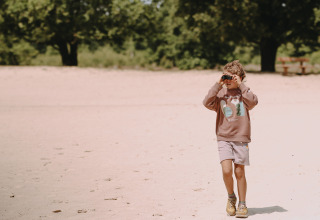 A child explores the sandy landscape near Fochteloo, Friesland, Netherlands, using binoculars.