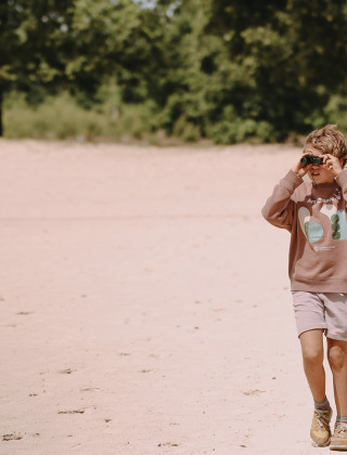 Een kind met een verrekijker wandelt door het zand bij Fochteloo in Friesland, Nederland.