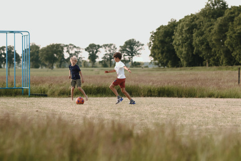 Twee kinderen spelen voetbal op een grasveld bij Feather Down De Appelsche vakantiepark in Friesland, Nederland.