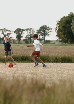 Twee kinderen spelen voetbal op een grasveld bij Feather Down De Appelsche vakantiepark in Friesland, Nederland.