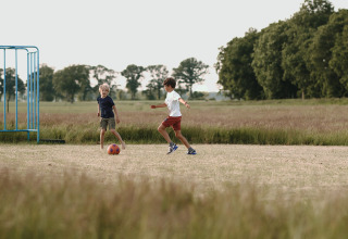 Twee kinderen spelen voetbal op een grasveld bij Feather Down De Appelsche vakantiepark in Friesland, Nederland.