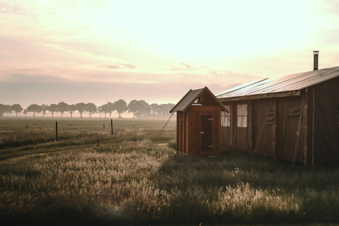 Solopgang over et telt ved Feather Down De Appelsche i Friesland, Holland, omgivet af natur og marker.