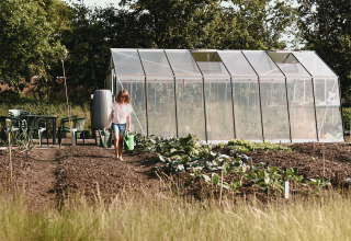 Een kind geeft de moestuin water voor een kas bij Feather Down De Appelsche, Friesland, Nederland.