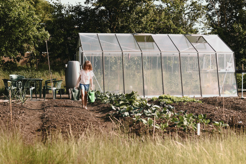 Un enfant arrose le potager devant une serre au Feather Down De Appelsche, parc de vacances à Friesland.