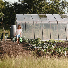 Een kind giet water in de moestuin bij een serre in Feather Down De Appelsche, Friesland, Nederland.