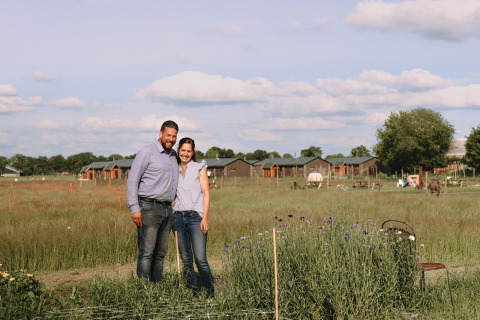 Una pareja de pie junto a flores y cabañas en el parque vacacional Feather Down De Appelsche en Frisia, Países Bajos.