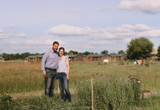 Una pareja de pie junto a flores y cabañas en el parque vacacional Feather Down De Appelsche en Frisia, Países Bajos.