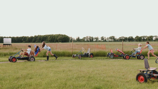 Kinderen en volwassenen racen en duwen gocarts op een grasveld bij Feather Down De Appelsche, Friesland.