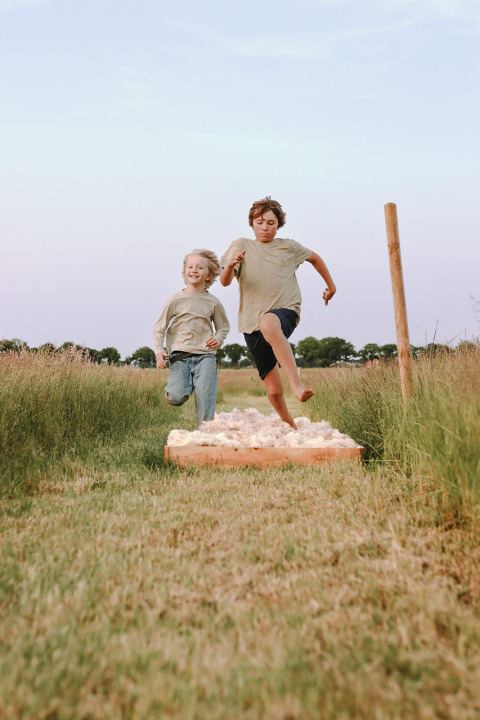 Twee kinderen springen over een hindernisbaan in het gras bij Feather Down De Appelsche, Friesland, Nederland.