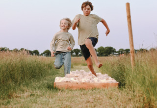 Twee kinderen springen op een hindernisparcours in het gras bij Feather Down De Appelsche, Friesland.