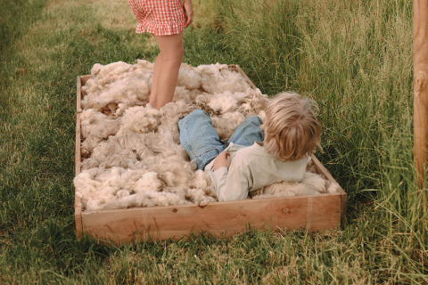 Twee kinderen spelen in een houten kist vol wol op het gras bij een vakantiepark in Friesland, Nederland.
