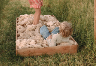 Two children play in a large wooden box filled with wool, outdoors at a holiday park in Friesland, Netherlands.