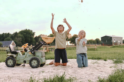 Twee kinderen spelen in het zand met een speelgoedtractor bij Feather Down De Appelsche, Friesland.