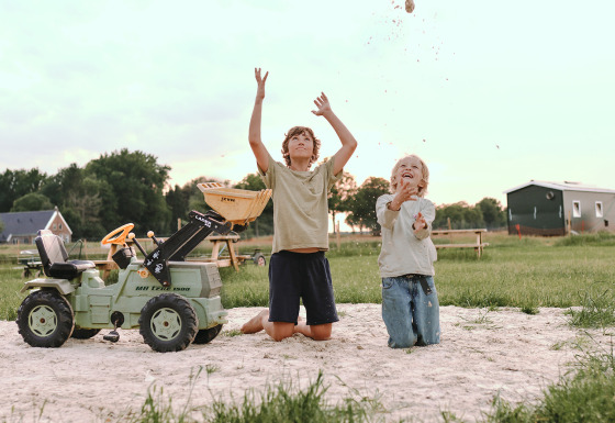 Dos niños juegan en la arena con un tractor de juguete en Feather Down De Appelsche, Friesland, Países Bajos.