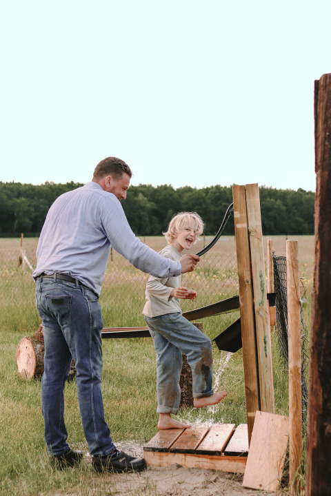Padre ayuda a niño sonriente a ducharse al aire libre en Feather Down De Appelsche, Friesland, Países Bajos.