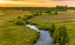 Vredig landschap rond Fochteloo, Friesland, Nederland met slingerende rivier en groene velden bij zonsondergang.