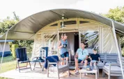 Famiglia si rilassa sulla terrazza arredata di una tenda glamping a Domaine des Messires, Grand Est, Francia.