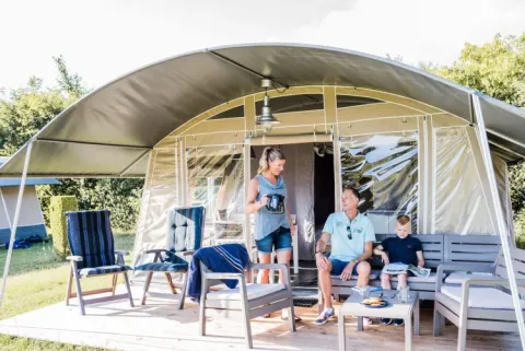 Famiglia si rilassa sulla terrazza arredata di una tenda glamping a Domaine des Messires, Grand Est, Francia.