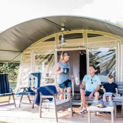 Family relaxing on a furnished terrace outside a glamping tent at Domaine des Messires, Grand Est, France.