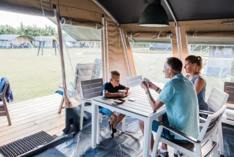 Familie, der spiller kort ved et bord i et telt på Domaine des Messires, en feriepark i Grand Est, Frankrig.