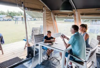 Familie, der spiller kort ved et bord i et telt på Domaine des Messires, en feriepark i Grand Est, Frankrig.