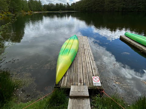 A green and yellow kayak lies upside down on a wooden dock by a calm lake at Domaine des Messires, France.
