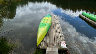 A green and yellow kayak lies upside down on a wooden dock by a calm lake at Domaine des Messires, France.