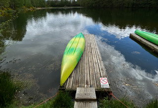 Un kayak verde e giallo capovolto su un pontile di legno vicino al lago nel Domaine des Messires, Francia.