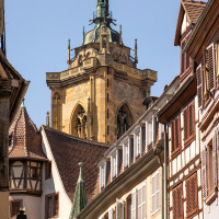 Street view near Herpelmont, Grand Est, France, with timber-framed houses and a historic church tower.