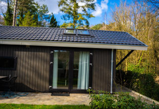 Bos Cottage en De Thijmse Berg, Países Bajos, con fachada oscura moderna y rodeado de árboles y naturaleza.