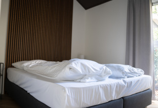 Cama doble con sábanas blancas en Bos Cottage, De Thijmse Berg, Países Bajos. Habitación moderna y luminosa.