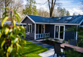 Buitenaanzicht van Heuvelrug Cottage + hot tub met terras, tuinset en omringd door bomen.
