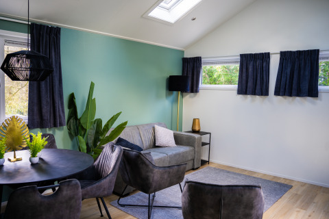 Moderne stue i Heuvelrug Cottage med grøn væg, sofa, spisebord og store vinduer på De Thijmse Berg, Holland.