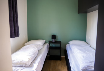 Dormitorio sencillo con dos camas individuales, mesita de noche y lámpara en Heuvelrug Cottage, De Thijmse Berg.