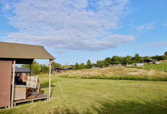 Uitzicht op een safaritenthuisje met privé hete douche bij de boerderij, omgeven door groene weilanden.
