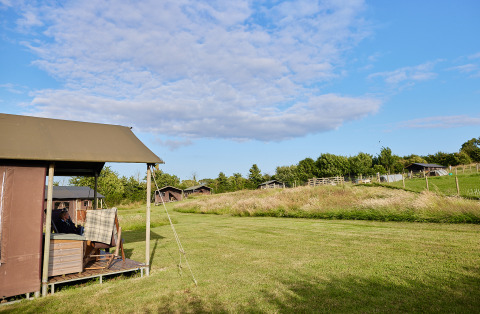 View of a safari tent cottage with private hot shower at a farmer's house, surrounded by green fields.