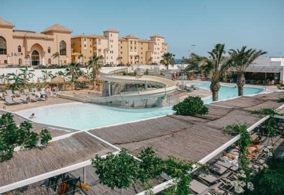 Zicht op zwembad met glijbaan, palmbomen en ligbedden bij Camping Costa del Sol Glamping Village, Andalusië.