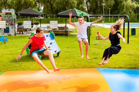Drie kinderen springen en spelen op een kleurrijk springkussen in vakantiepark De Scherpenhof, Gelderland.