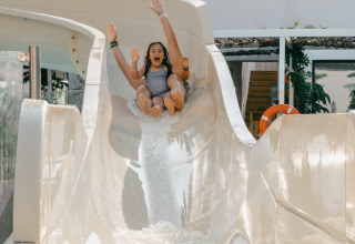 Two joyful people sliding down a waterslide at Camping Costa del Sol Glamping Village, Andalusia, Spain.