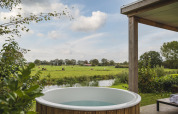 Udendørs badekar med udsigt over grønne marker, en dam og køer ved River Lodge 'Wellnesshuus', Mölke, Holland.