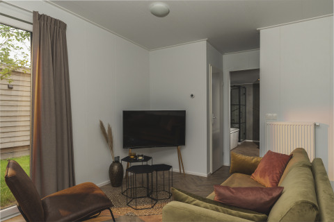 Acogedora sala de River Lodge 'Wellnesshuus' en Holiday Park Mölke, Países Bajos, con sofá, TV y ventanal al jardín.