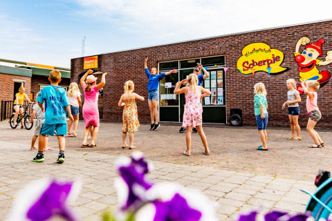 Kinderen dansen vrolijk buiten bij Kinderclub Scherpje in vakantiepark De Scherpenhof, Gelderland, Nederland.