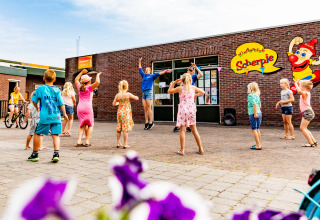 Kinderen dansen vrolijk buiten bij Kinderclub Scherpje in vakantiepark De Scherpenhof, Gelderland, Nederland.